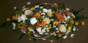 Orange, yellow, white and green funeral display. Gem stones placed in the centre of some flowers and white winter berries make a respectful statement